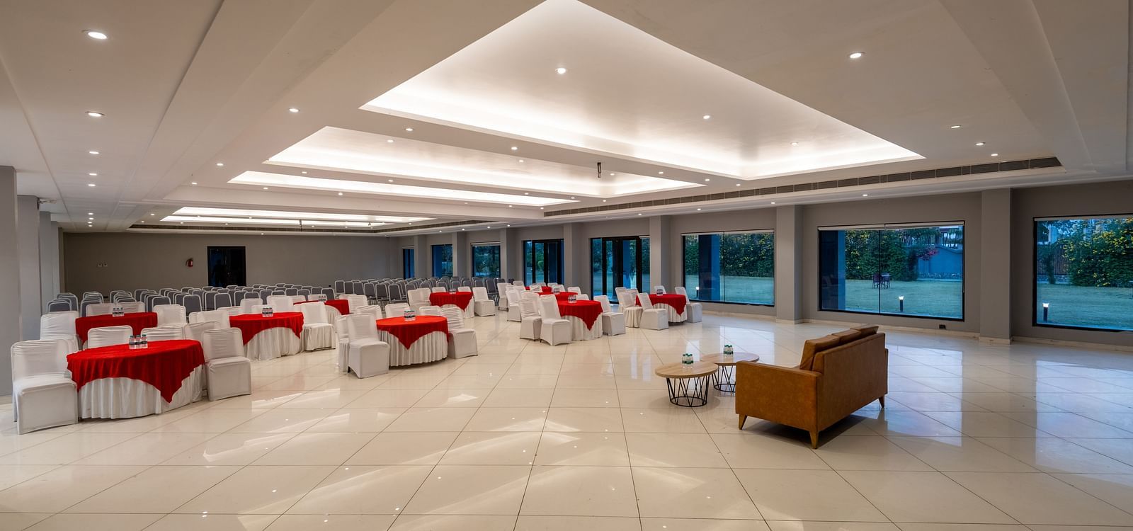 Side view of tables with neatly decorated tablecloths, a plush sofa, and two round tables set in front at DLS Forest Vines Resort.